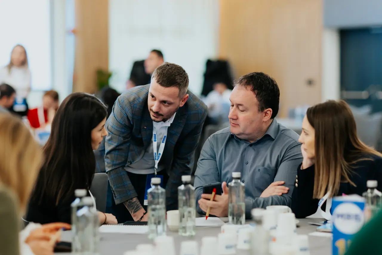 Participant aplecat spre colegi într-o discuție la masă, MRB 2025