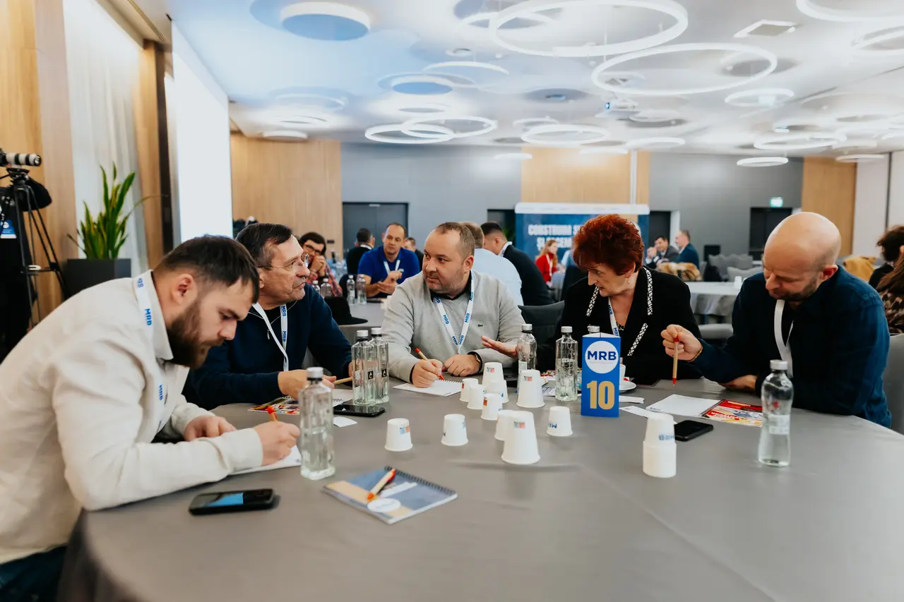 Participanți lucrând pe fișe la o masă cu moderator, MRB 2025