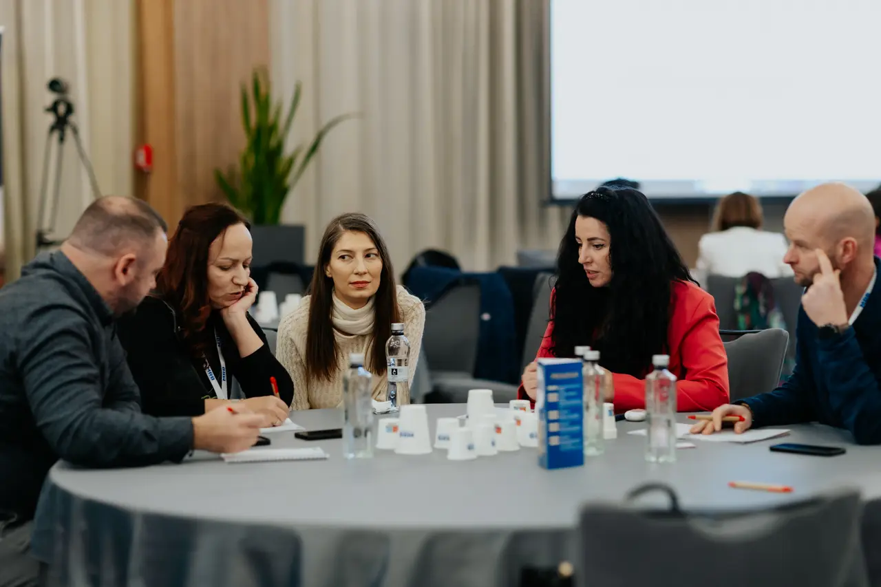 Grup de participanți lucrând pe fișe la o masă rotundă, MRB 2025