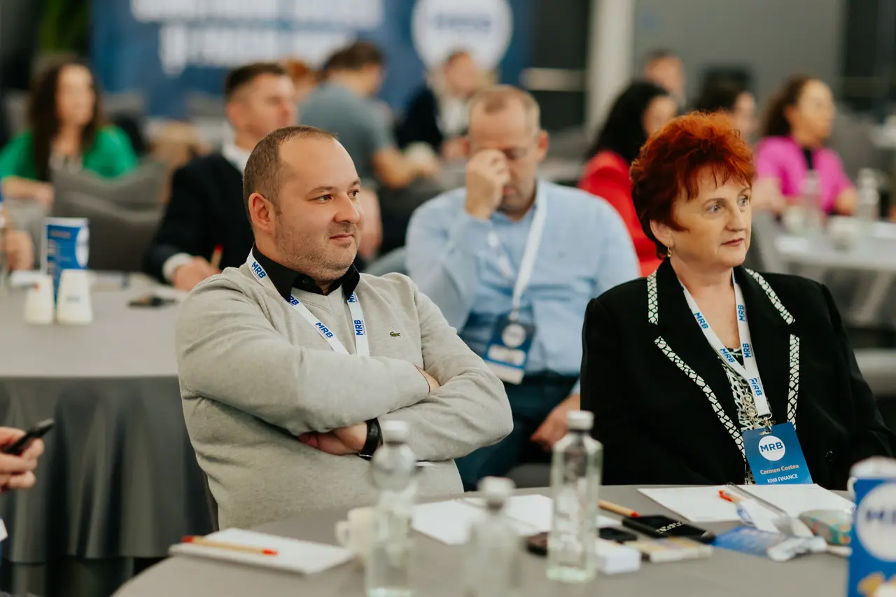Doi participanți zâmbind la masă în timpul prezentării, MRB 2025